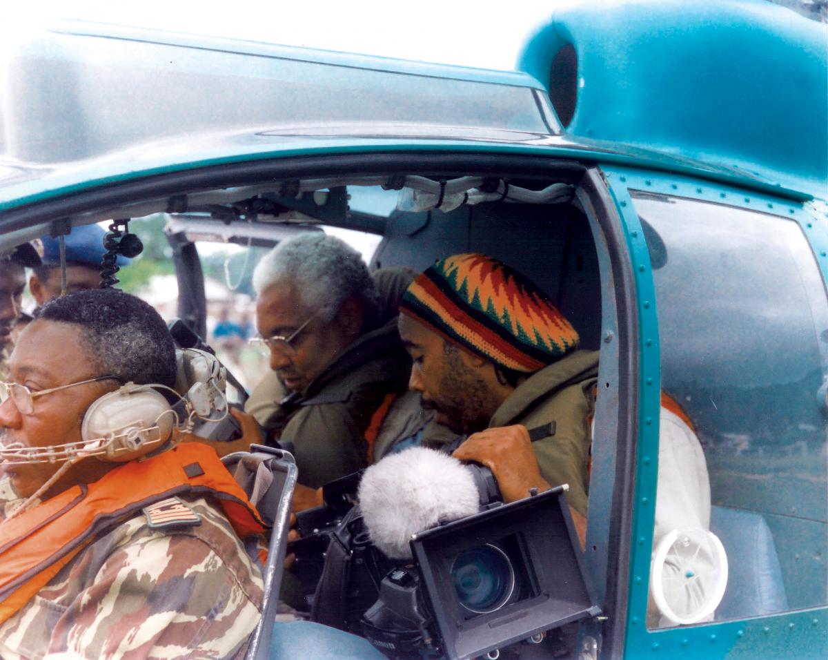 Collinet sits in a packed car, looking down at a camera, while his companions look on