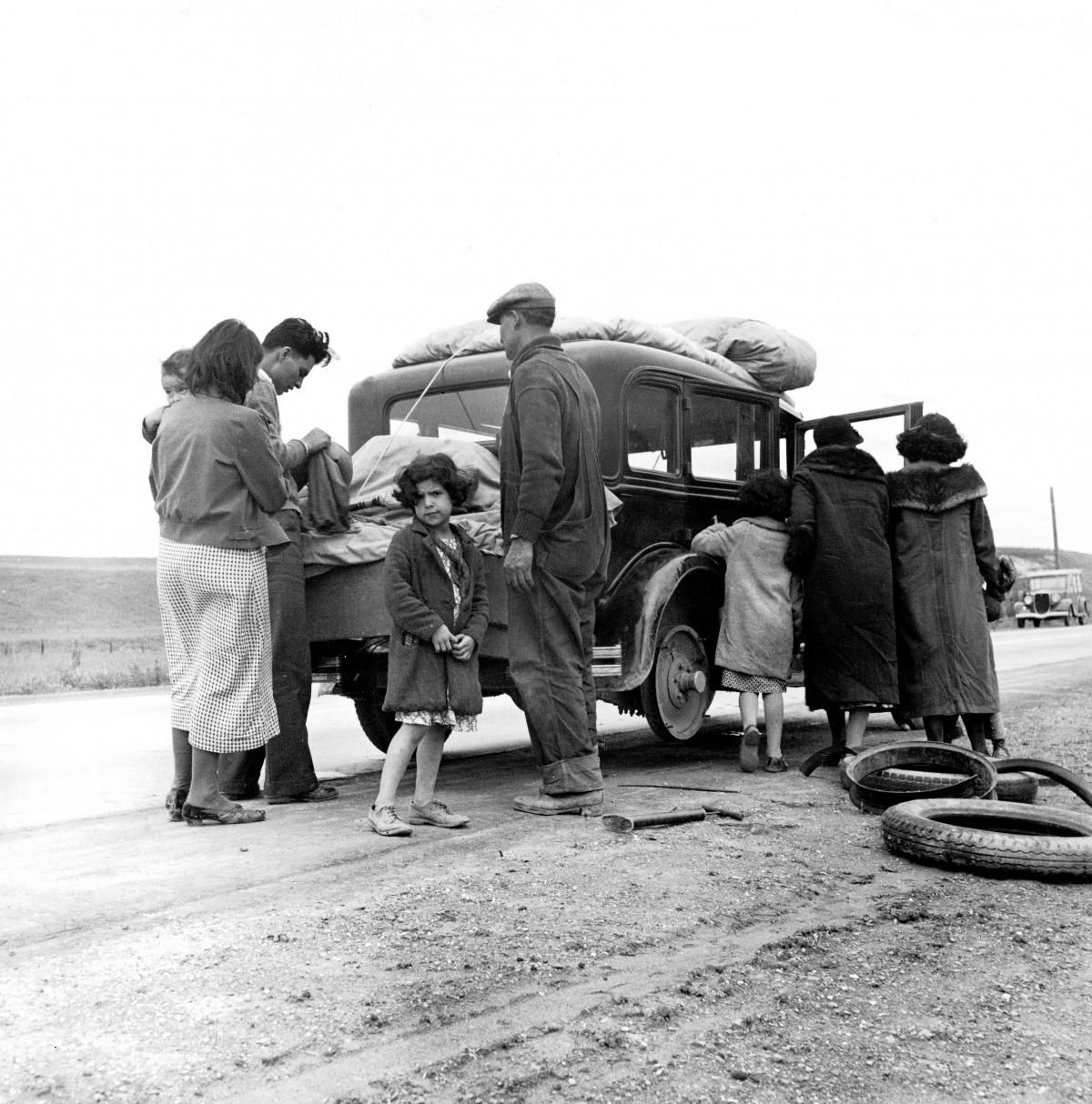 family gathered around car, discarded tire on ground