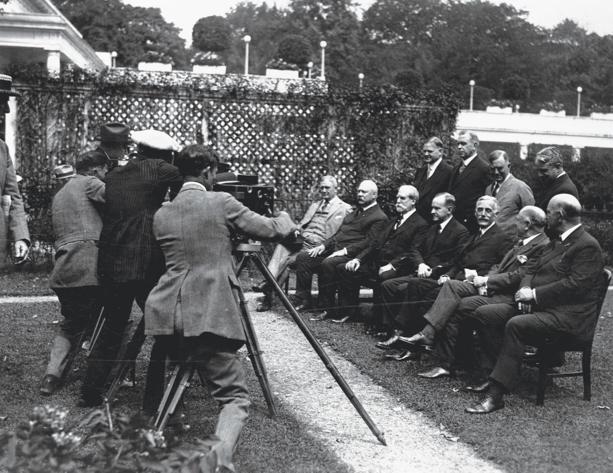 black and white group photo of men in suits sitting down in front of camera