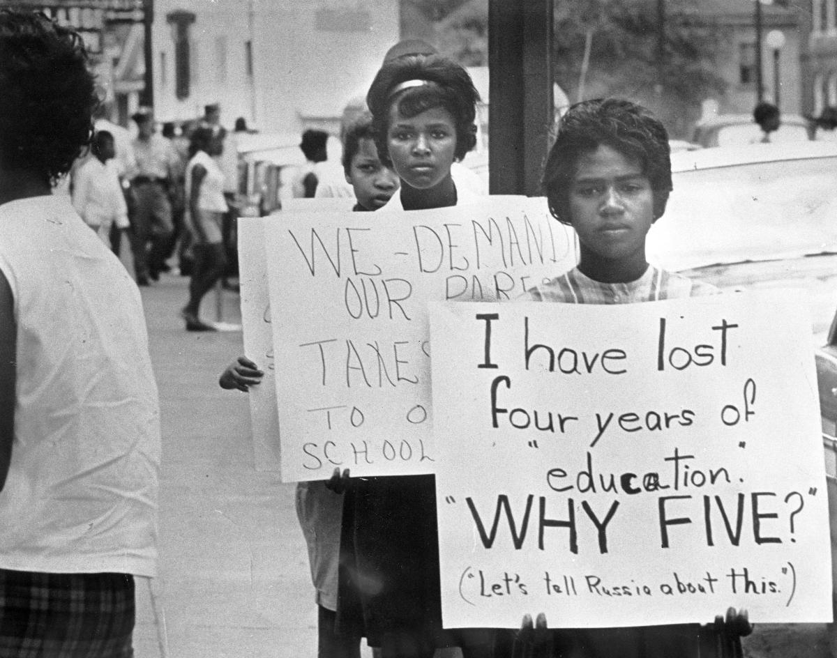 Two young African American women hold protest signs questioning the school closure