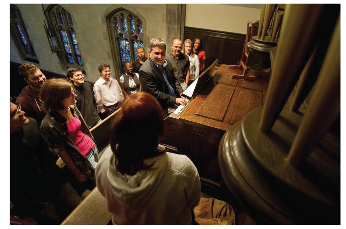 Clavere teaching his students about a wooden pipe organ