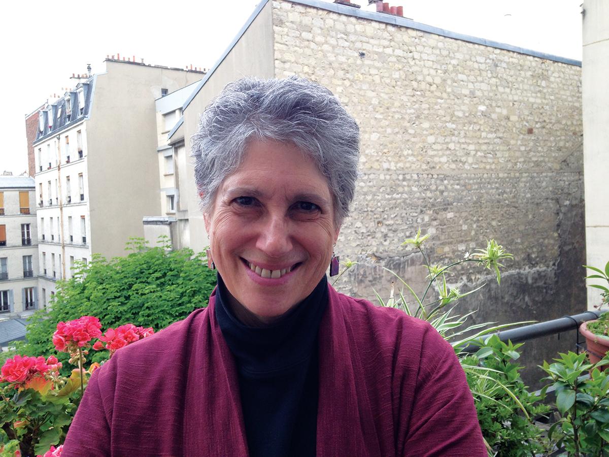 Ellen Gruber Garvey in a purple sweater, standing on a balcony above bushes