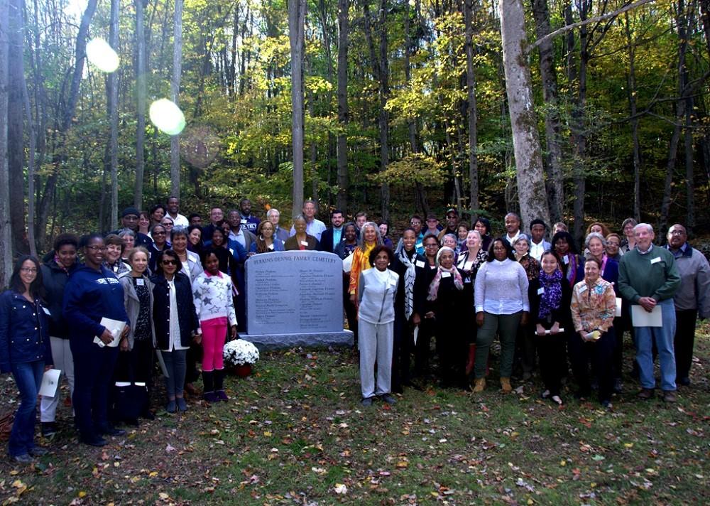 Ten members of the Dennis family stand with visitors in front of the Perkins-Dennis Family Cemetery Monument during an event held at Dennis Farm.