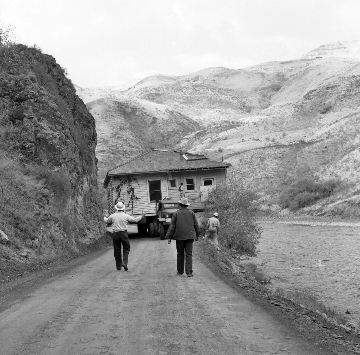 Black and white photo of men moving a house on a tractor.