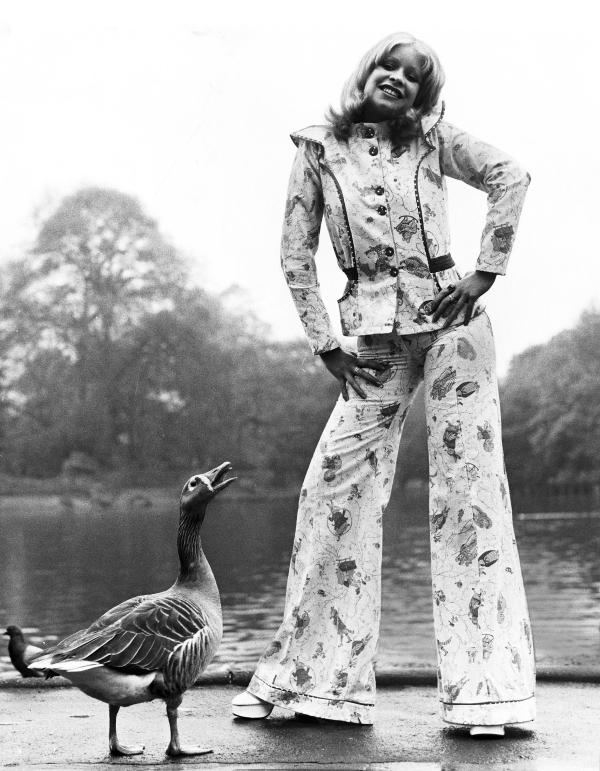 Woman models a pantsuit made of fabric decorated in Beatrix Potter characters. She's being eyed by a nearby goose.