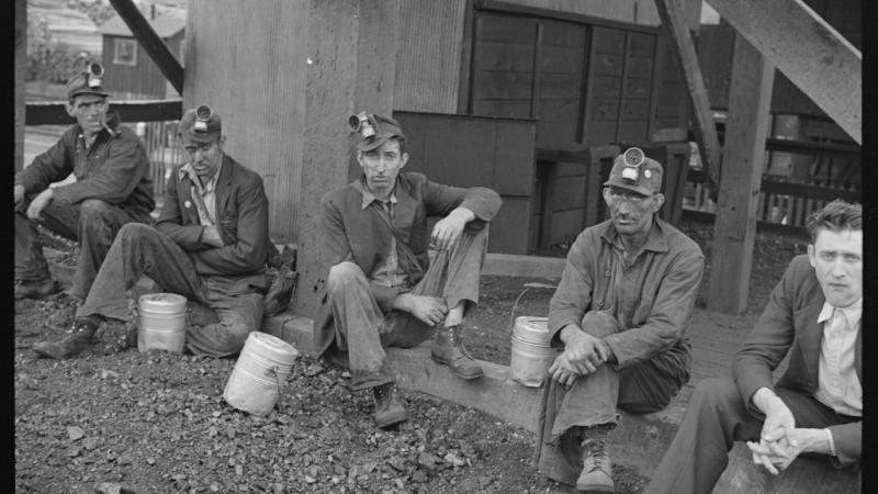 Black and white photo of five coal miners sitting on ground